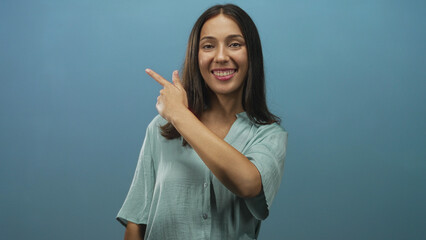Woman points finger to right while smiling in studio against a soft blue backdrop; cheerful...