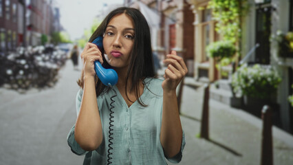Woman holds blue handset to ear on busy city street with parked bicycles and flowered storefronts;...