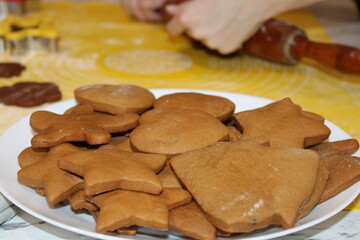 Baking gingerbread cookies in the kitchen with rolled dough on a yellow surface and cookie cutters in use