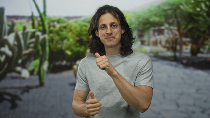 Fototapeta premium Man gives thumbs up and points finger toward left in street with green park behind him; optimism connection.