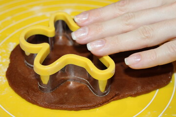 Hands using a cookie cutter to shape dough on a yellow mat in a kitchen setting during a baking session
