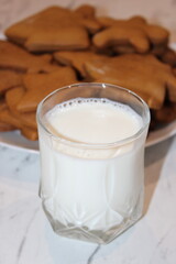 Milk and cookies on a white table with baked goods in the background during an afternoon snack time