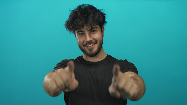 Young hispanic man with beard smiling and pointing at camera against blue background creating a friendly inviting atmosphere. - Powered by Adobe
