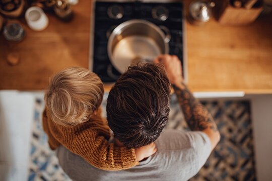 Dad stirs a pot on the stove while holding a young child in his arms, showcasing parental bonding