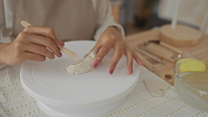Young blonde woman hands shaping clay on pottery wheel in studio; creativity focus craftsmanship calm.