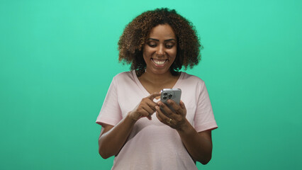 Woman tapping smartphone with fingers, smiling and looking down in a teal studio; digital connection joy engagement.