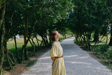 Obraz premium woman outdoors park portrait with yellow dress on a gravel path in a lush environment serene sunlight textures and greenery under trees creating a peaceful summer mood