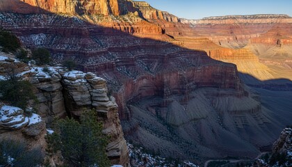 Vast layered red rock canyon landscape with a dusting of winter snow on the cliffs, illuminated by the warm golden light of a dramatic sunrise