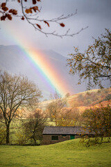 A vibrant rainbow slices through the overcast sky on an autumnal day in the picturesque Lake District, Ambleside, United Kingdom.