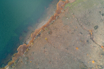 Aerial top down view of lake shoreline with brown reeds and dry grass field. Autumn nature water texture and river bank landscape background