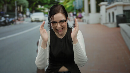 Fototapeta premium Brunette woman outdoors on the street makes a size gesture using her hands with expressions of surprise and focus, set against a blurred urban background.