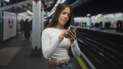Woman scrolling smartphone with fingers at a subway platform inside building while checking...