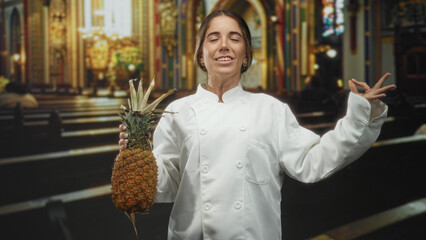 Woman chef holding pineapple with meditative hand gesture and closed eyes in a building; culinary ritual serenity.