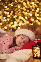 Little cute girl sleeping under Christmas tree and dreaming of Santa cooming. Happy kid child waiting for gifts on xmas.