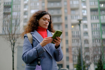 Woman using smartphone standing in city, low angle