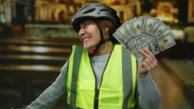 Hispanic senior woman wearing a helmet and reflective vest holds american dollars joyfully inside a church, highlighting themes of cycling and wealth. - Powered by Adobe