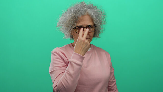 Elderly woman with grey hair gesturing vigilance against a green background, wearing glasses and a pink sweater, adds an intriguing focus to social awareness.