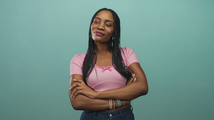 Woman with arms crossed and head tilted upward in studio, wearing pink top and jeans, bracelets and necklace visible; thoughtful contemplation.