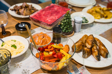 Festive home dinner table with fried carp, roasted vegetables, layered beetroot salad, and classic holiday dishes creating a warm family celebration mood with seasonal food traditions.