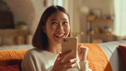 A cheerful Asian woman excitedly holding a smartphone, filled with happiness. The scene exudes warmth and joy Stock Video