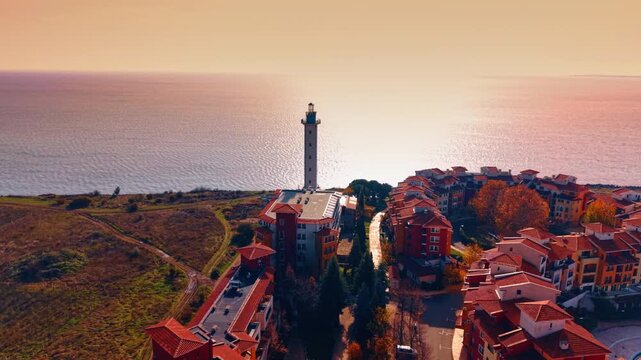 Tower of Aheloy lighthouse against seascape dazzled with bright setting sun. Drone footage over the lovely colorful houses. Bulgaria.