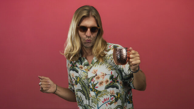 Blond man dancing with copper mug and sunglasses in a pink studio setting with long hair flowing to the side; holiday joy fun celebration. - Powered by Adobe