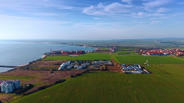 Flying over green fields approaching water treatment plant. Residential area of Aheloy, Bulgaria at the sea coast at backdrop.