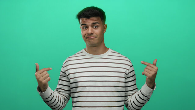 Young man in striped shirt gestures over isolated green background, looking puzzled and confident, expressing indifference and calm, conveying a relaxed mood. - Powered by Adobe