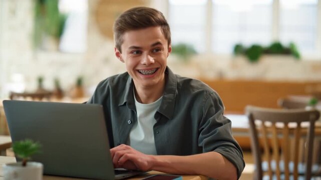 A young man happily working on a laptop at a cafe. The setting is bright and casual, conveying a sense of productivity and contentment Stock Video