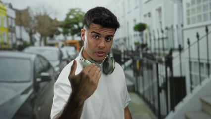 Obraz premium Young man with headphones standing on a city street surrounded by parked cars and buildings.