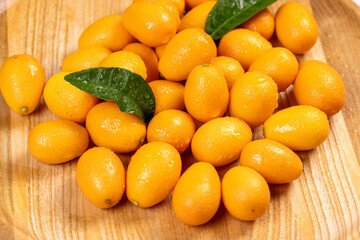 Fresh wet kumquats with leaves on wooden tray