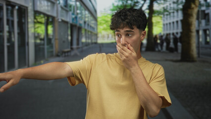 Fototapeta premium Man points finger on a city street beside trees and modern buildings, arm extended in a casual pose; curiosity discovery.