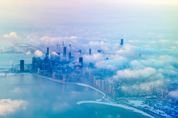 Aerial view of Chicago, Illinois, featuring iconic skyscrapers like Willis Tower and John Hancock Center amidst cloud cover. The skyline is partially obscured by clouds, creating an ethereal scene