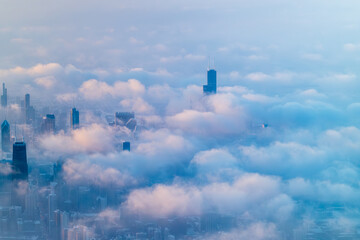  Chicago's skyline with skyscrapers emerging through dense cloud cover. Several iconic buildings partially obscured by soft, low-lying clouds during winter at golden hour sunrise