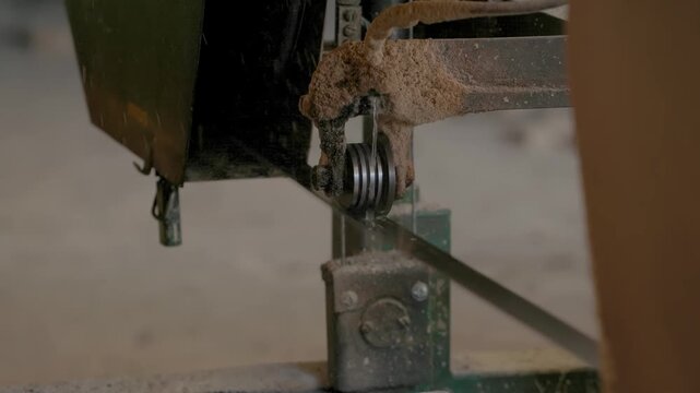 Close-up of dusty bandsaw guide system with vertical blade and metal wheels, green frame suggests active use in workshop setting.