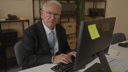 Senior man in a business suit working at a computer in an office, showcasing a professional indoor workplace environment.
