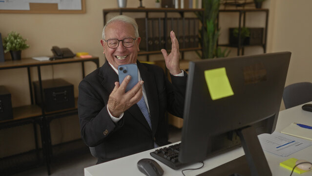 Senior man in business suit using smartphone and computer in modern office interior, appearing focused and engaged at the workplace with shelves and a neat desk. - Powered by Adobe