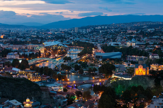 Aerial View Of Illuminated Tbilisi Cityscape With Bridge Of Peace At Dusk