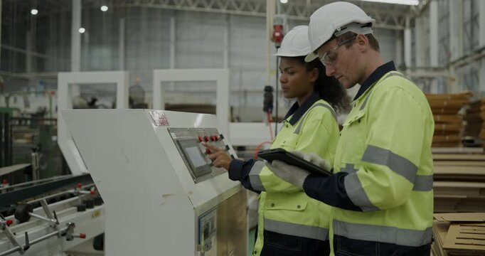 Industrial concept of 4k Resolution. Engineers are inspecting a cardboard cutting machine in the factory with strict attention to safety procedures.