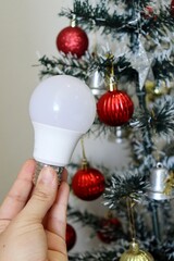 Hand holding LED light bulb with decorated Christmas tree in background. electricity bill concept during the Christmas holiday. 