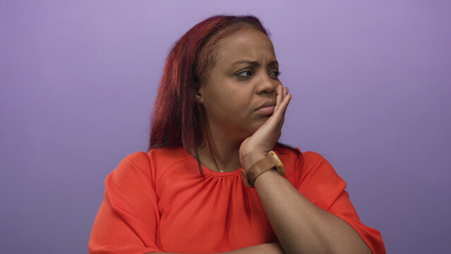 African american woman with red hair holding chin with hand against purple studio backdrop; reflection. - Powered by Adobe