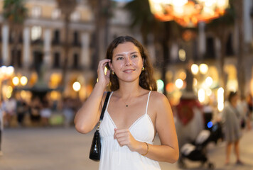 Obraz premium Long-haired cheerful female brunette walks along city street, spends time in motion, walks and enjoys sunny warm day, walks from university to home. Carefree, evening cafe, promenade. ..