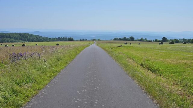 Strasse durch eine weitl&auml;ufige Landschaft mit gr&uuml;nen Wiesen und entfernten H&uuml;geln unter blauem Himmel, Koppelhutweg, Lange Rh&ouml;n, Hausen, Rh&ouml;n, Bayern, Deutschland, Europa