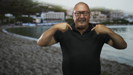 Man points both index fingers to chest while wearing black polo at a building by the shore; confidence affirmation.