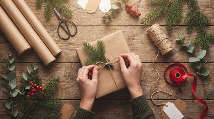 Wrapping gifts with brown paper and twine on a wooden table during the holiday season with scissors and decorations nearby