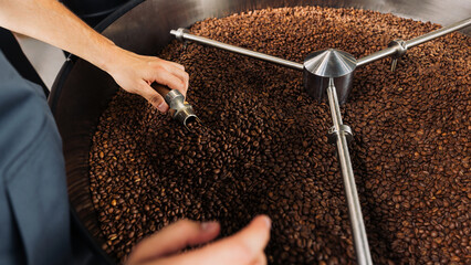 Hands of an unrecognisable barista checking the quality of coffee at the roasting drum
