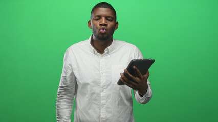 Man holds tablet with both hands and taps screen with finger in green studio; focused concentration.