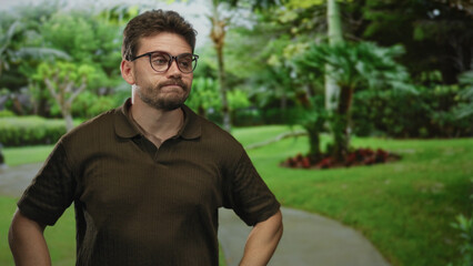 Man raising right hand in a green park pathway wearing glasses and polo shirt, looking up;...