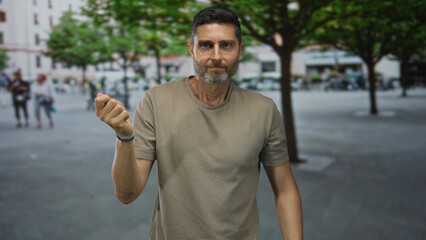 Naklejka premium Man points finger forward with bare hand in urban street plaza near trees and benches;determination accountability.