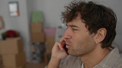 Obraz premium Man talking on phone in new home surrounded by moving boxes, indicating a fresh start and communication in a residential setting.